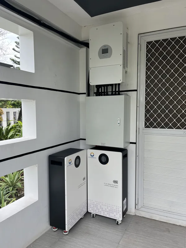 Hybrid inverter, protection enclosure and two battery cabinets beside a lattice door